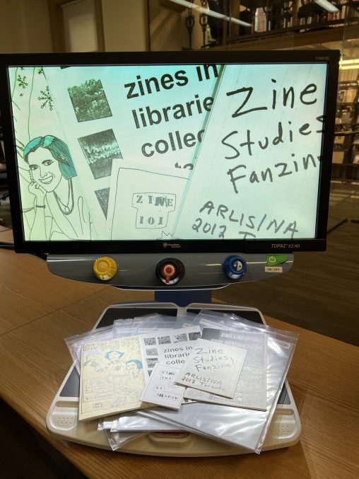A CCTV reader with an array of zines on it's tray. These zines are all about librarianship.